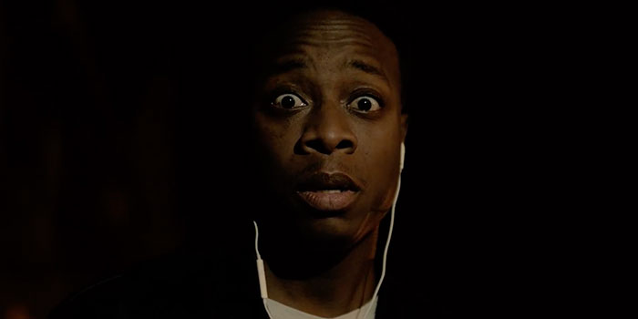 picture of a man in the dark, he is wearing headphones and looking at the camera terrified
