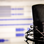 black microphone sitting in front of a blurred computer screen that has a white background and blue lines of different sizes on it