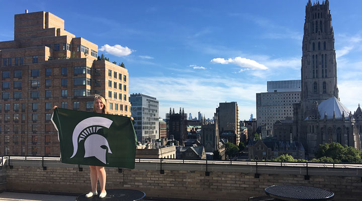girl standing on table with green and white flag with spartan head on it with NYC in the background
