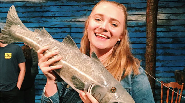 a girl with blonde hair wearing a jean jacket holding a fish