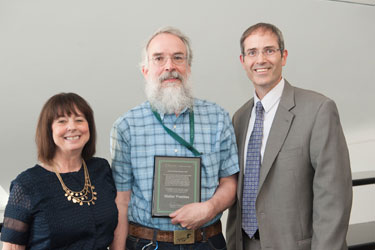 man smiling with award with a man on one side of him and a woman on the other