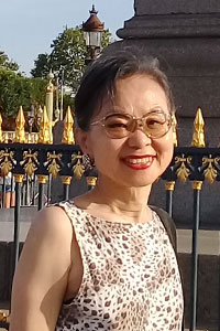 woman who's wearing glasses and a white and black patterned shirt who's standing in front of a black and gold fence outside