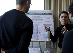 the back of two men looking at a women give a presentation on a poster behind her