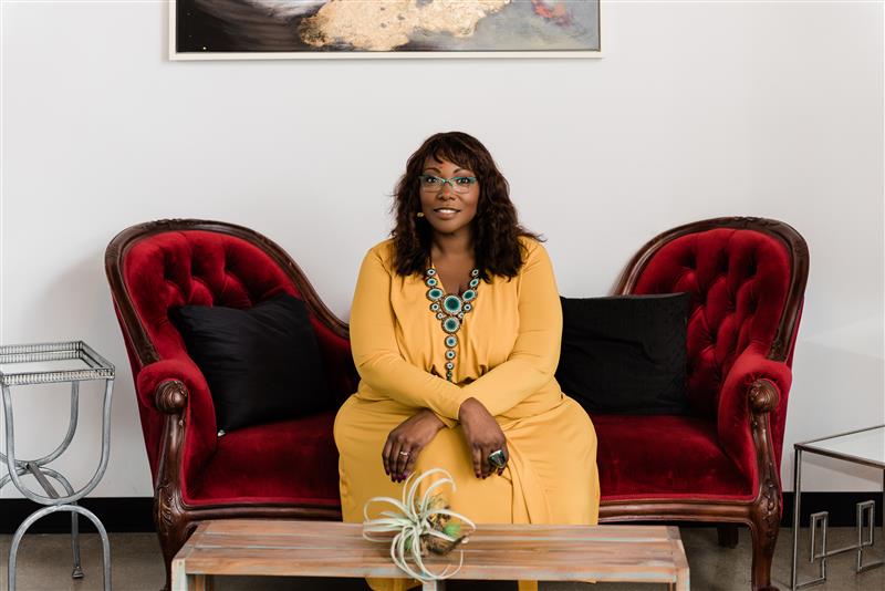 Woman in a yellow shirt and glasses sitting on a red velvet couch
