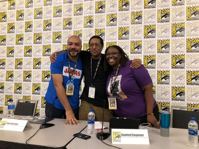 Three people embracing each other at a Comic-Con booth