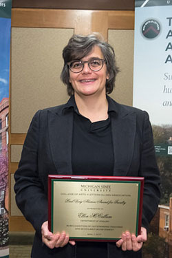 woman wearing glasses, a black shirt and jacket holding up an award