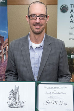 a man wearing glasses and a gray jacket holding up an award