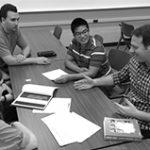 5 people sitting around a table discussing the paper on the table