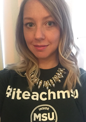 selfie of a woman with shoulder-length blonde hair, she is wearing a necklace and a t-shirt that reads "#iteachmsu"