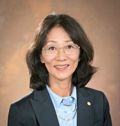 a woman with short dark hair wearing glasses and a navy blue blazer with a light blue shirt