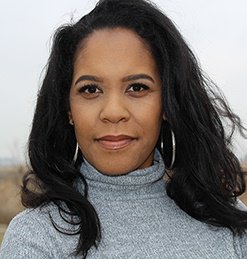 headshot of a woman with medium-length hair. she is wearing a gray turtleneck and hoop earrings