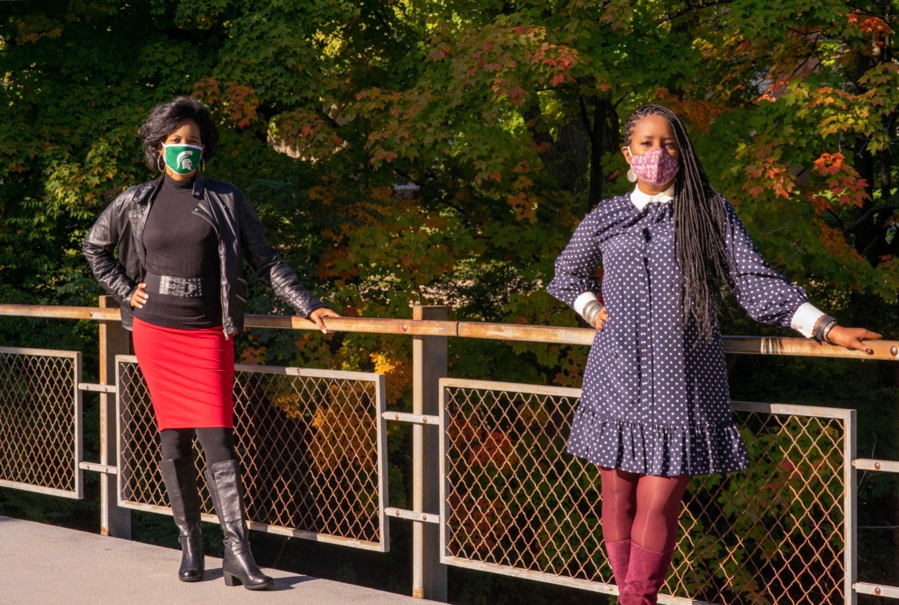 two women standing on a bridge wearing masks