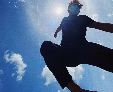 photo of a man wearing a mask doing jumping in the air with a bright blue sky with clouds in the background