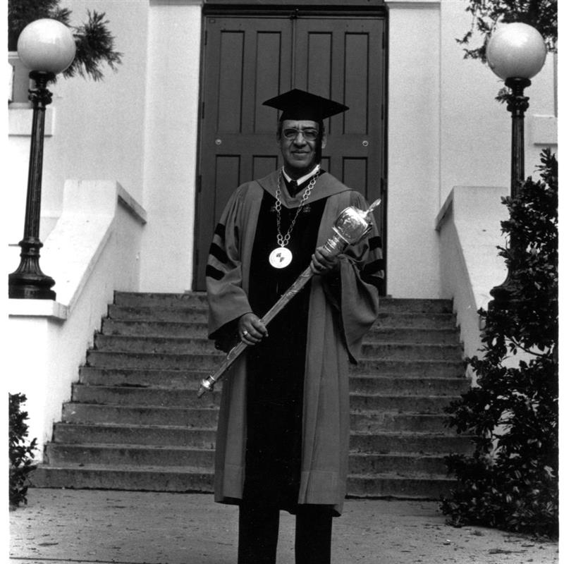 a black and white image of a man in a faculty grad cap and gown