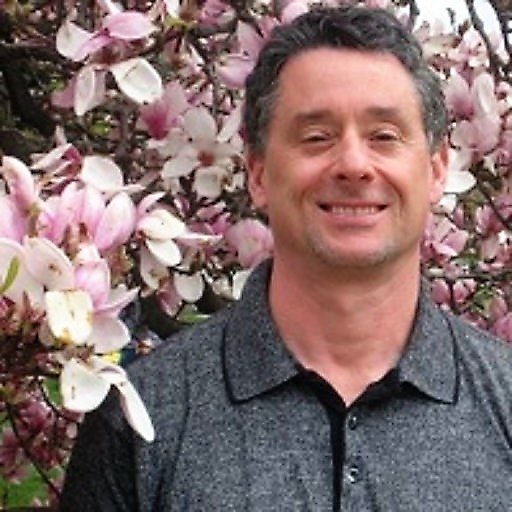 man wearing a gray shirt standing in front of a tree with pink and white flowers