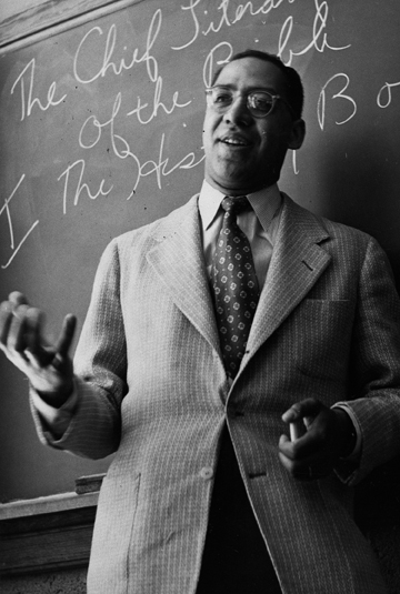 a black and white image of a man wearing glasses and a suit in a class room