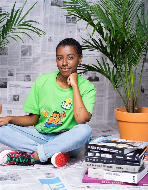 a person with short hair wearing a green shirt with blue jeans sitting with a stack of books next to them
