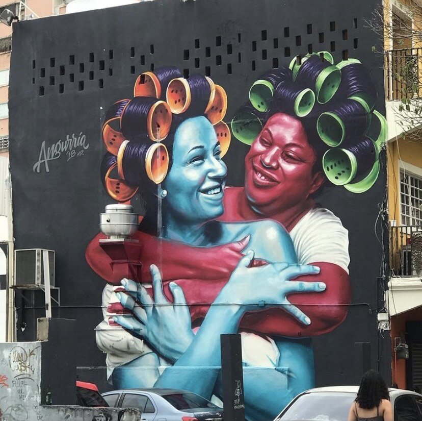 painting on a wall of a vlue woman and a pink woman embracing