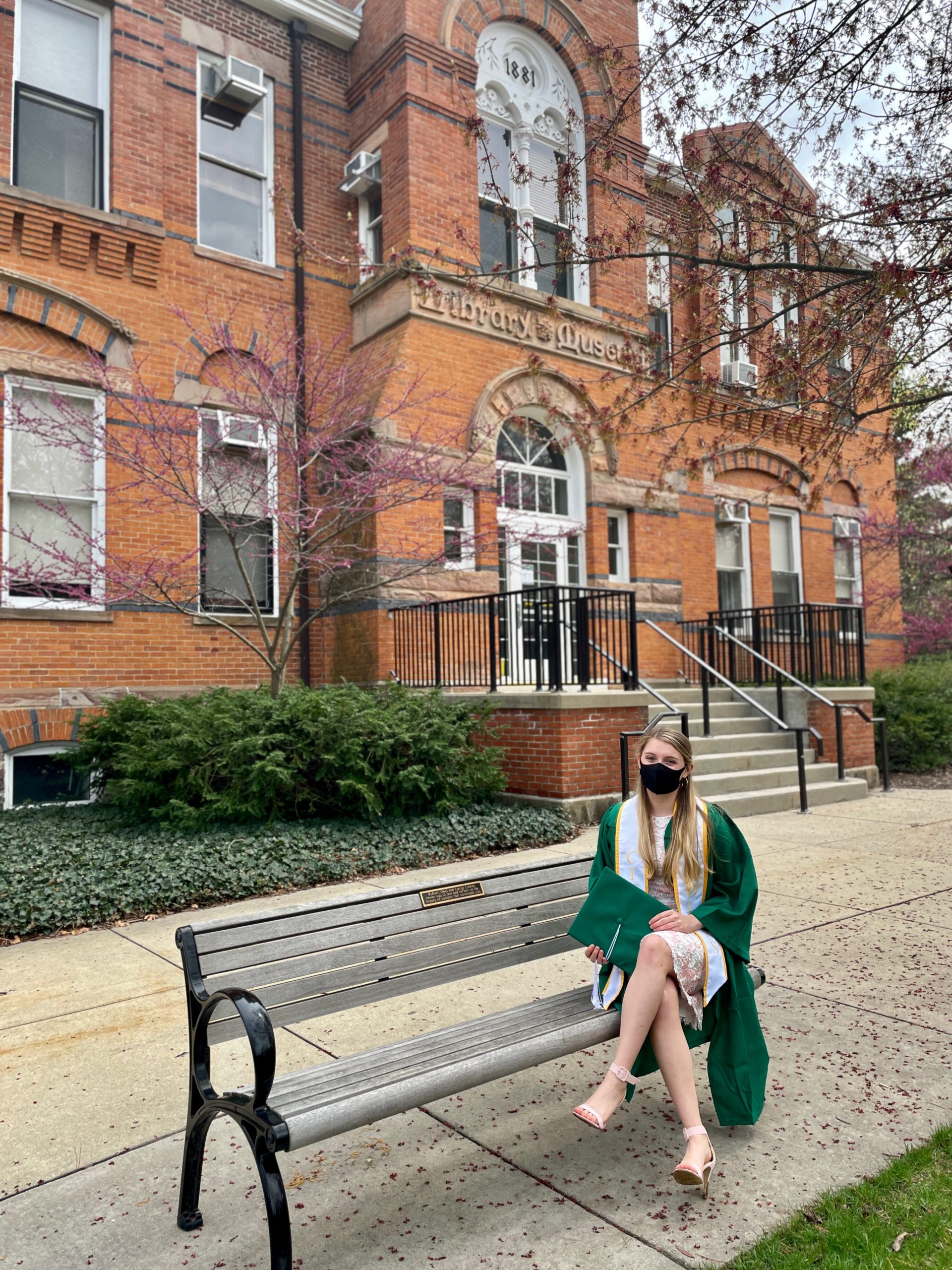 a girl with long blonde hair wearing a green gown sitting on a bench
