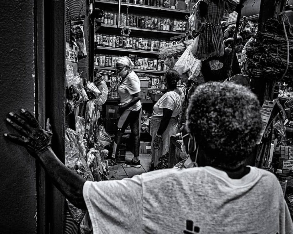 black and white image of someone looking into a room with the shelves stocked with things and people waiting in line