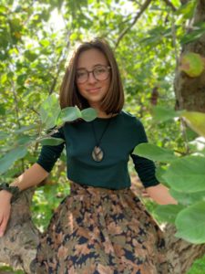 woman wearing glasses and a green shirt and floral skirt standing in trees