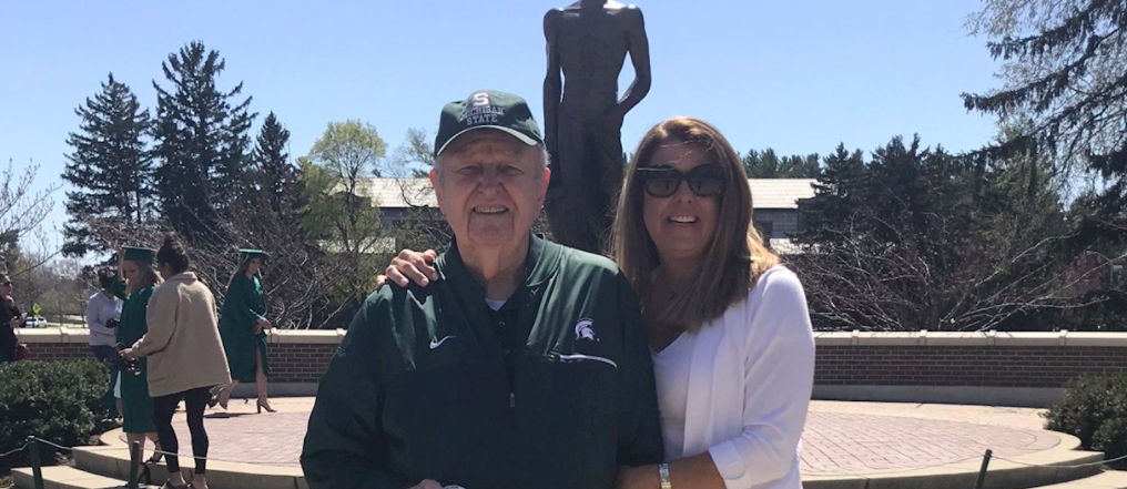 Man and woman standing side by side in front of the Spartan statue