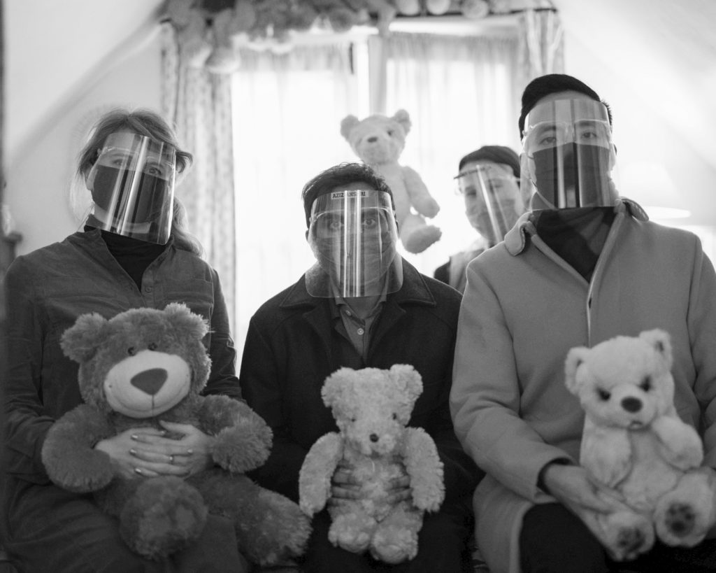 Three people sitting side by side wearing face masks and holding teddy bears