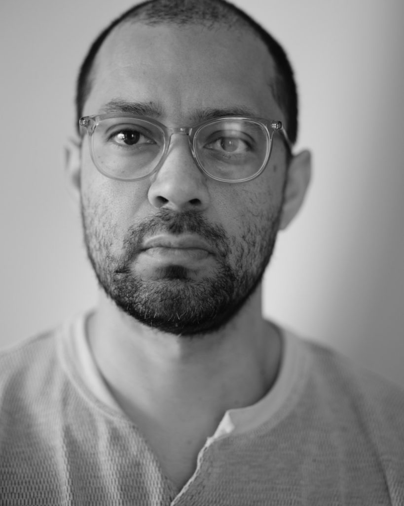 Black and white close-up of a bearded man with short hair and glasses.