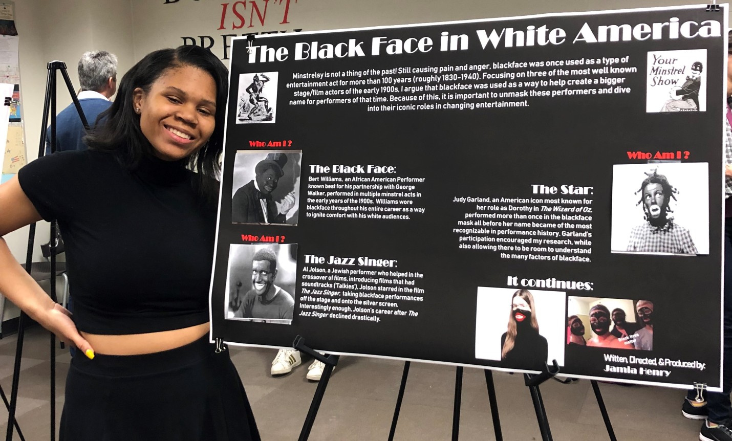 Woman wearing black standing next to a poster board