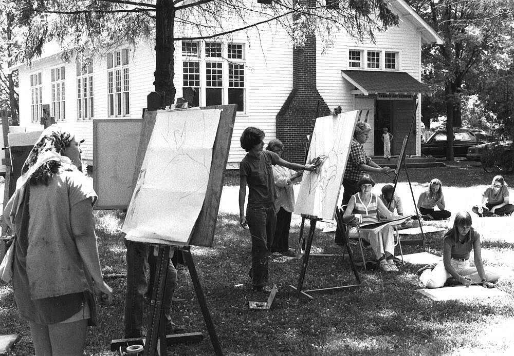 A group of people are outside painting on easels.