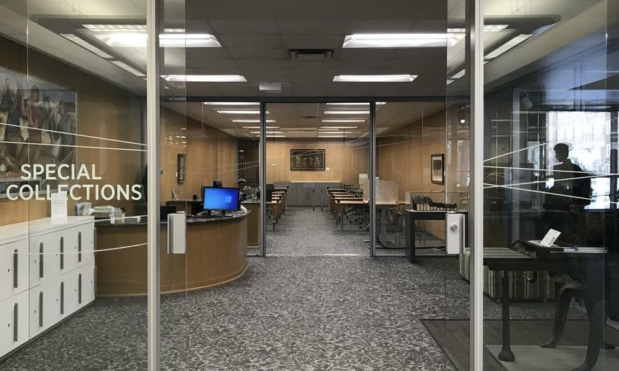 A photo of glass doors with the words 'Special Collections' on the left leading into a small lobby with another pair of glass doors leading into an area with desks and chairs.