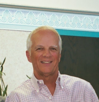 A picture of a man with short grey hair and a pink shirt smiling at the camera
