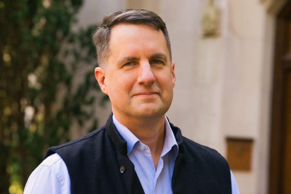 A portrait of a white man with short hair dressed in a button-down and vest.