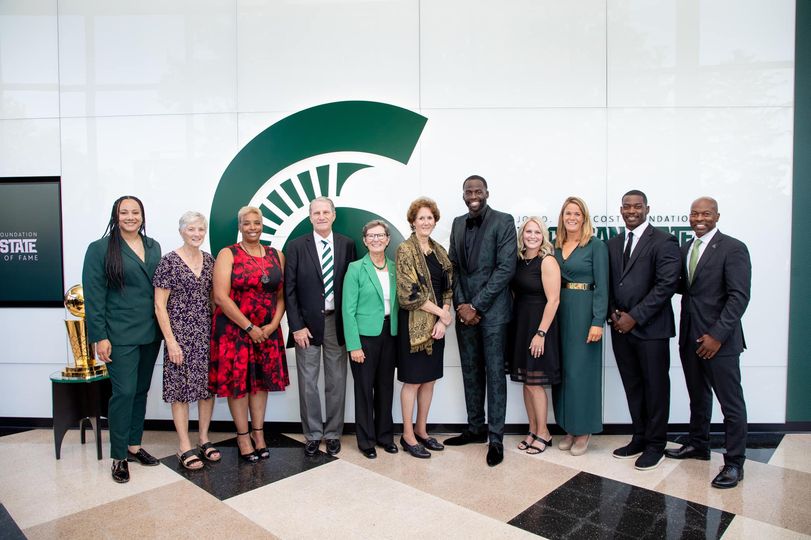A group of people in suits and dresses standing in front of an MSU logo.