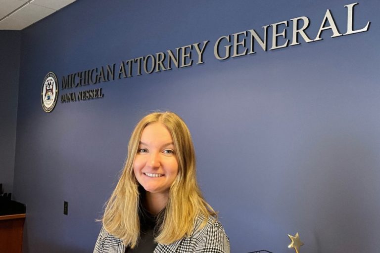 Blonde woman standing in front of a blue wall with Michigan Attorney General Dana Nessel logo