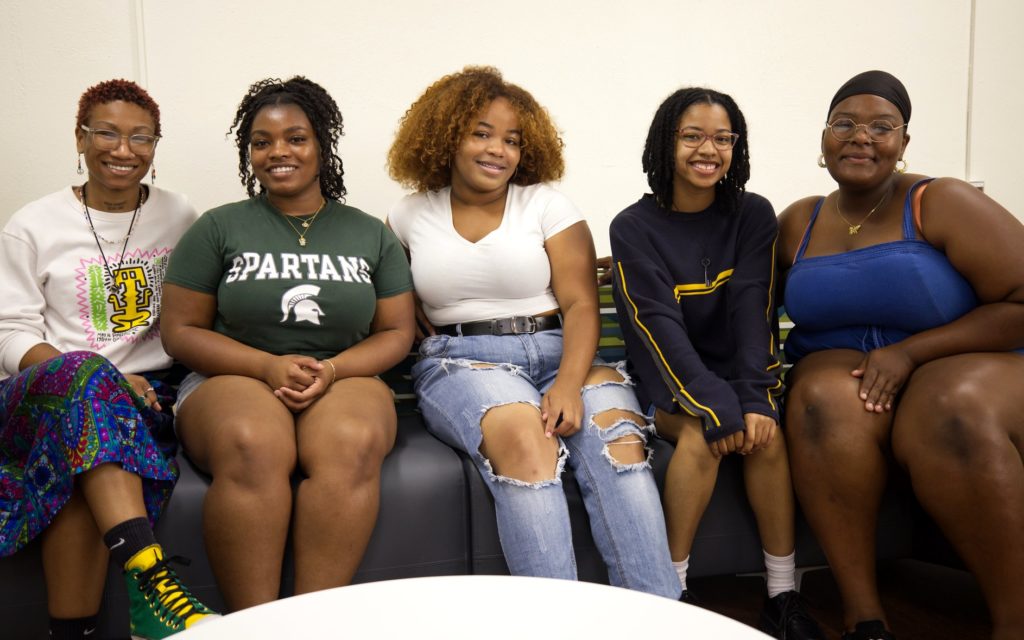 Five girls sitting on a couch smiling.
