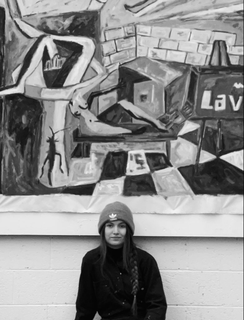 A black and white picture of a woman with a tall painting in the background. 