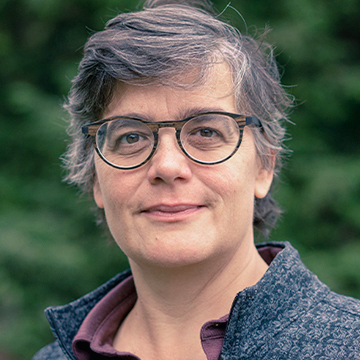 A picture of a woman with short grey hair and glasses smiling at the camera. 