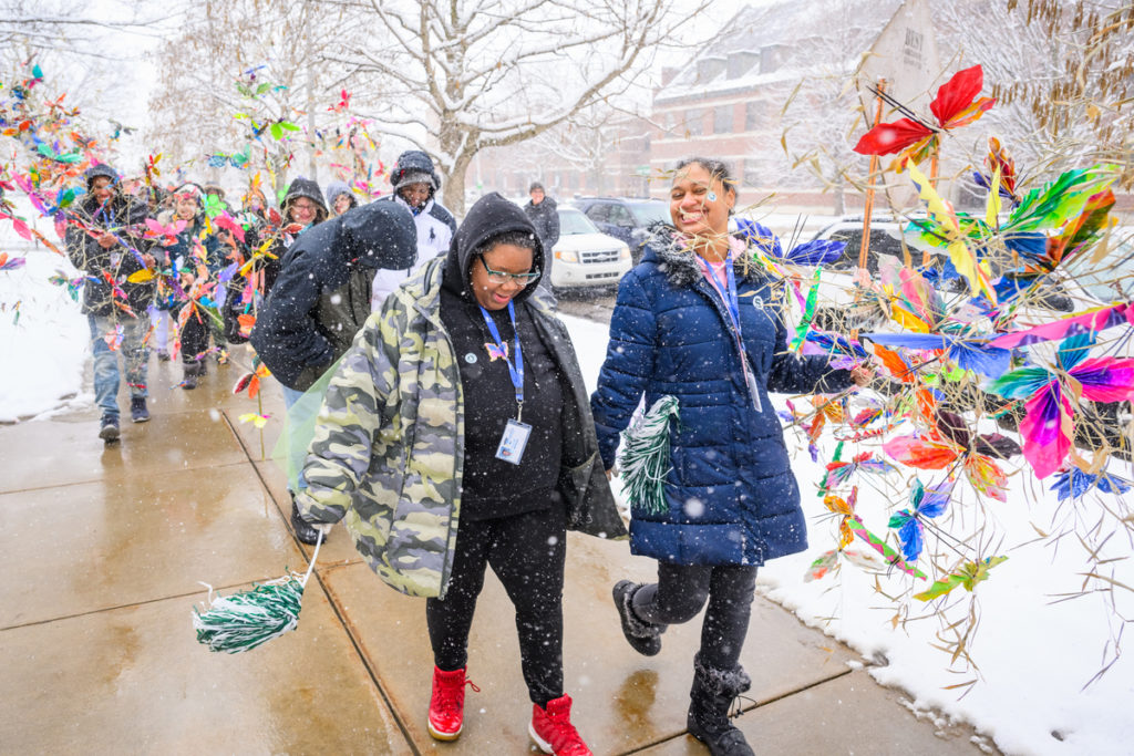 A picture of a group of students carrying large, colorful sculpture pieces in the snow. 