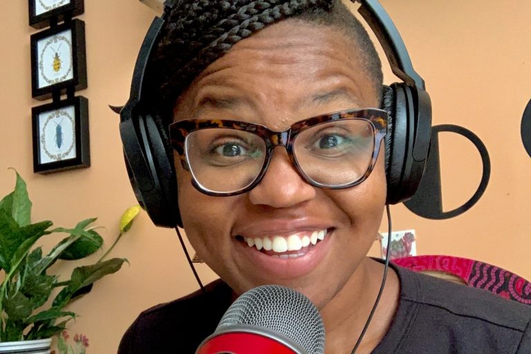 Close up portrait of a person wearing headphones and smiling behind a large microphone.