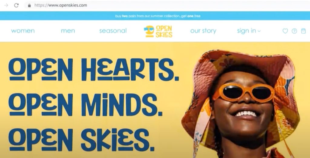 The Open Skies website's front page with a smiling woman wearing a bucket hat and sunglasses on the right and the words "Open Hearts. Open Minds. Open Skies." on the left.