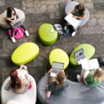A bird's-eye view of a group of students sitting around green stools.