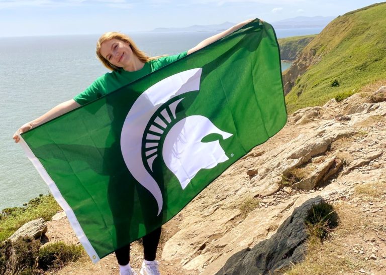 Person standing on water horizon holding green spartan logo flag.