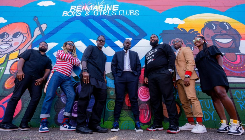 A group photo with 7 people pictured in front of a mural that says "Reimagine Boys & Girls Clubs."