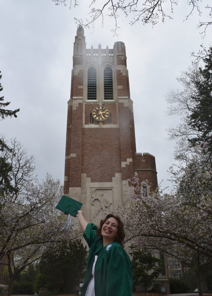 Photo of Julianna Bruno wearing a cap in gown in front of Beaumont Tower.