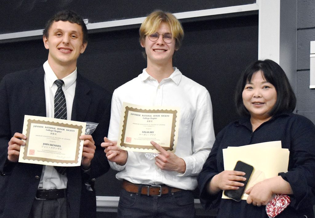 Two students smile with a University Professor after receiving their award. 