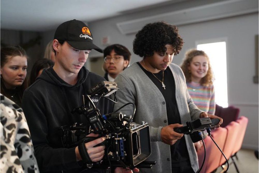 Two students in the foreground handle film equipment while five stand in the background behind them.