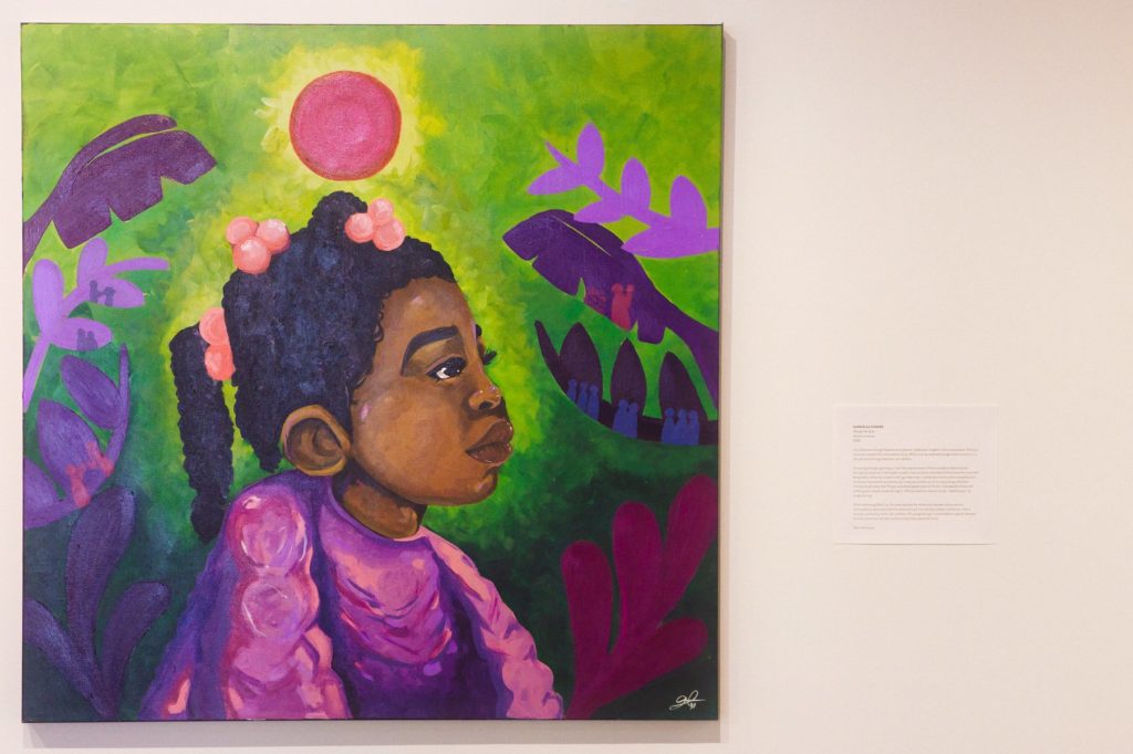 Photo of a painted portrait of a little black girl with a background of leaves.