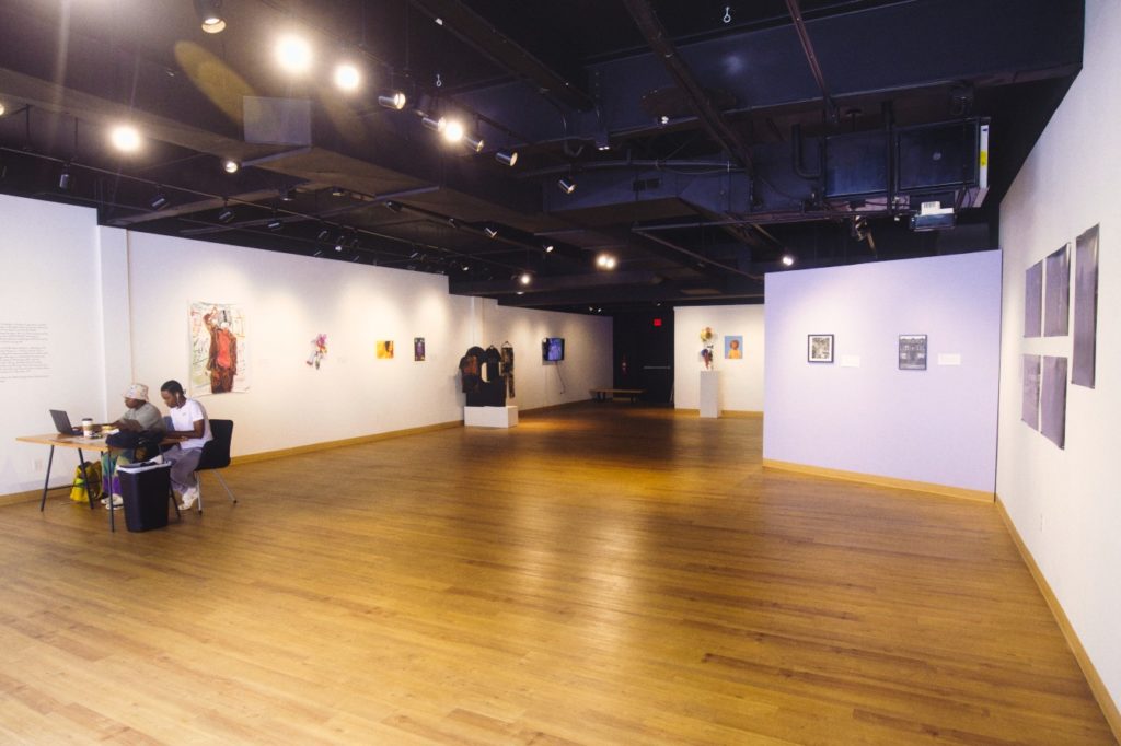 Photo of an art gallery with wooden floors and photos displayed on the walls.