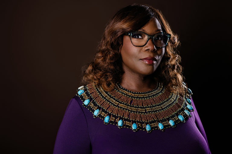 Portrait of a woman wearing glasses, a purple dress, and a colorful necklace.